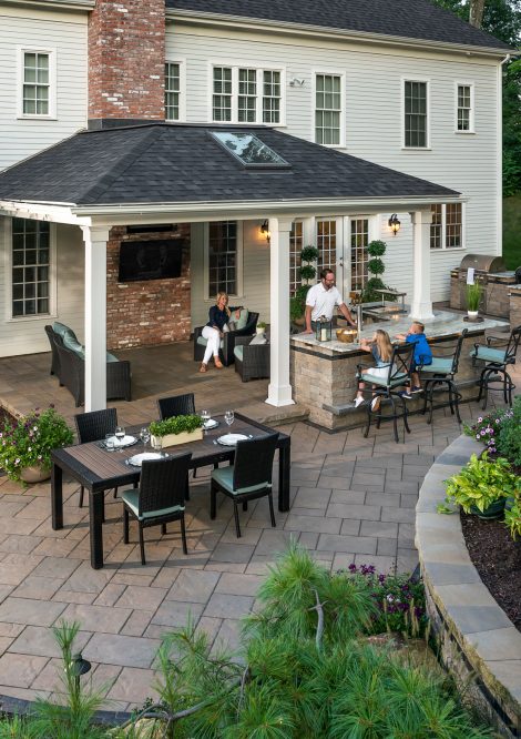 Family sitting around Outdoor Kitchen Island under Gazebo with TV wall